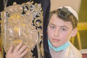 Bar Mitzvah Joseph au Luxembourg gros plan sur le visage de Joseph avec le téfiline sur le font serrant de près la Torah. Photographe à Metz