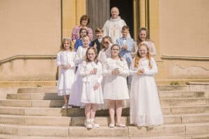 Photo officielle sur les marches de l'église : les 10 enfants entourent le prêtre et Mme Valérie Lieber pour un souvenir de groupe a retonfey en 2025.