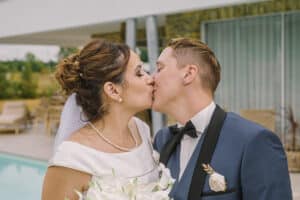 Mariage de Marie et Priscilla à la Villa St Andrews : les deux mariées partagent un baiser passionné devant la piscine, Priscilla en costume bleu et Marie en robe de mariée blanche