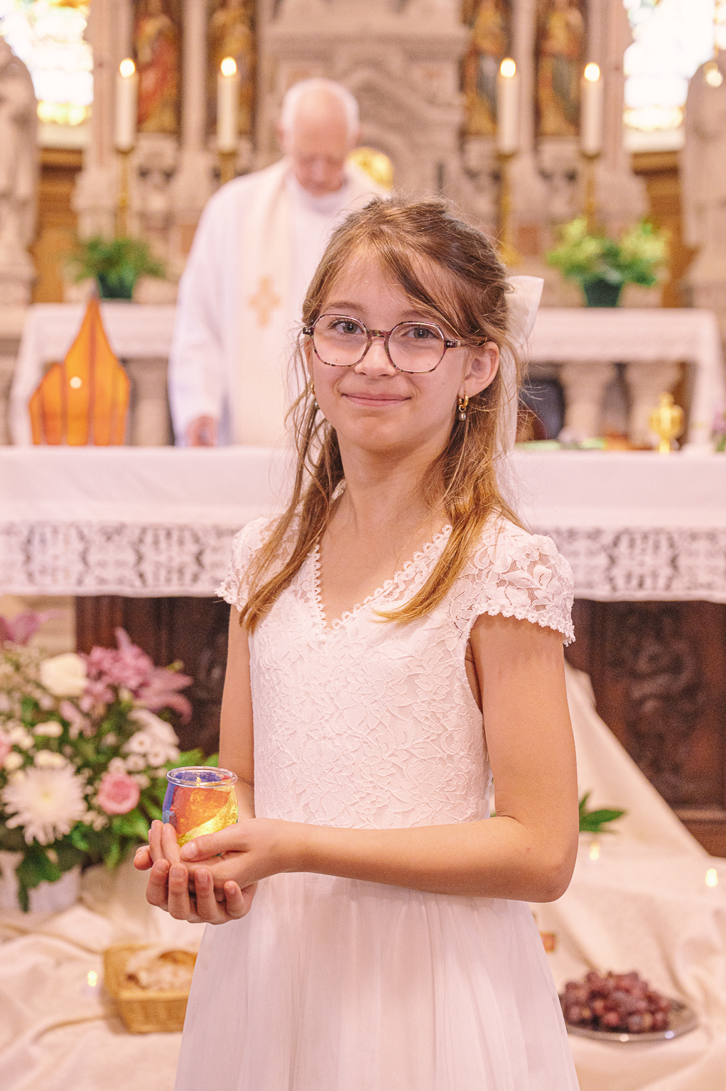 Jeune fille en robe blanche tenant une photophore colore devant l'autel lors de sa premiere communion