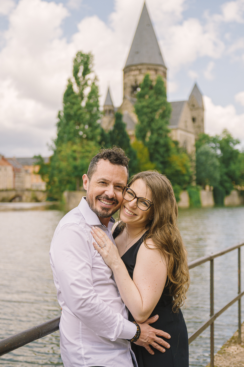 Portrait rapproche d'un couple souriant enlacé au bord de l'eau devant un bâtiment historique