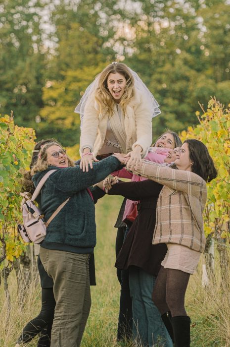 Copines portant la future mariee avec voile au-dessus de leurs têtes au milieu des vignes